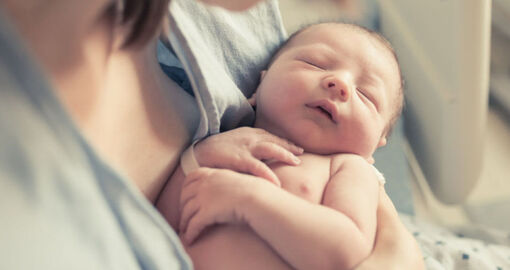 Ein neugeborenes Baby liegt in den Armen der Mutter. 